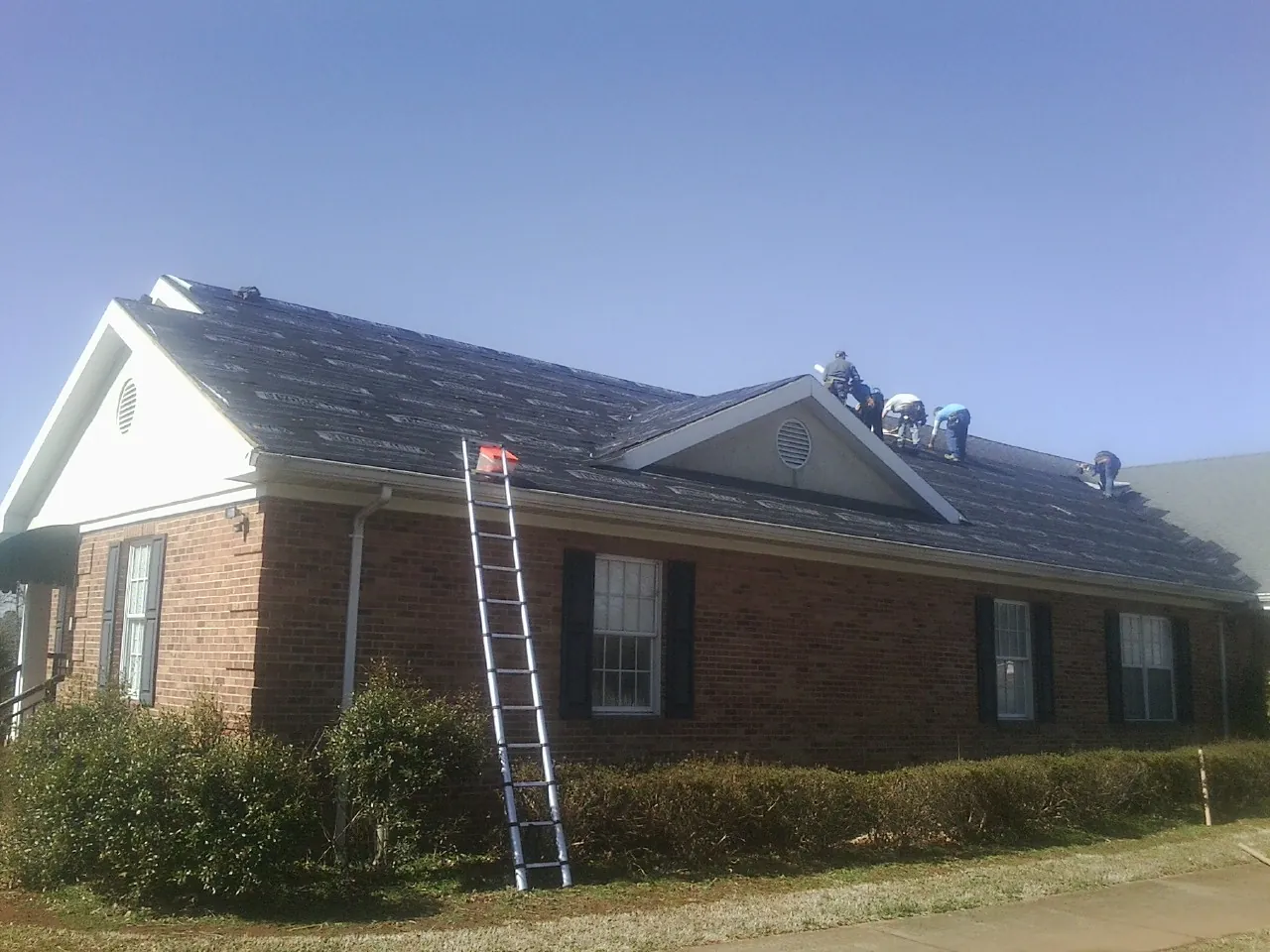 Crew tearing shingles off a brick ranch roof with a ladder set — Emergency Roof Repair work by our crew in Five Points