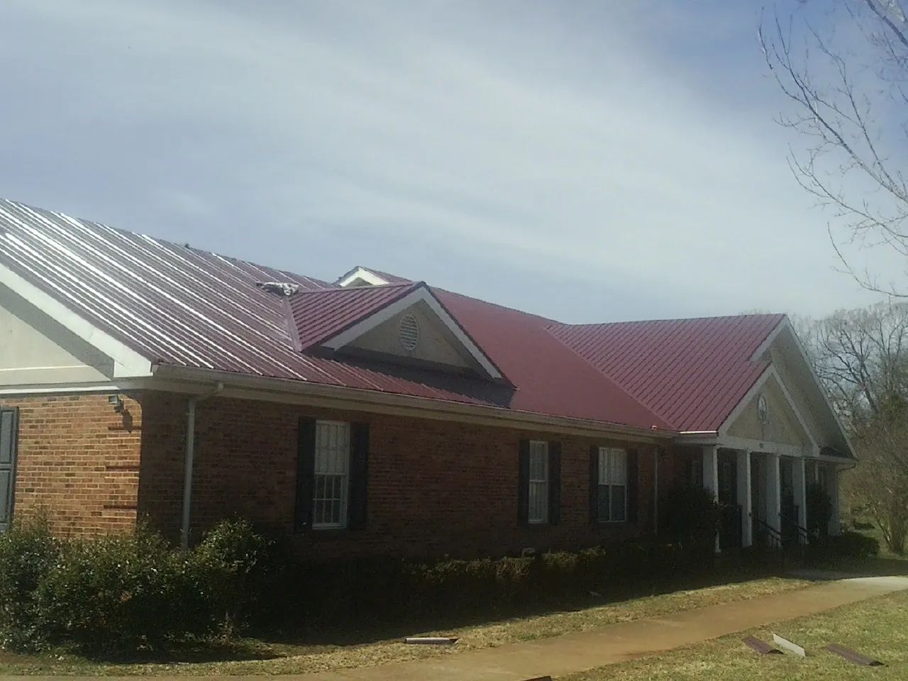Red metal roof with gabled entries on a long brick building, from a Hail Damage Roof Repair job in Five Points