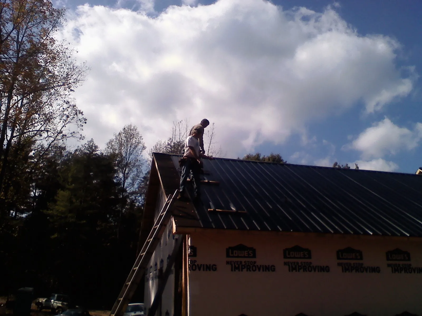 Roofer fastening dark metal panels high against a cloudy sky, from a Roof Inspection job in Five Points