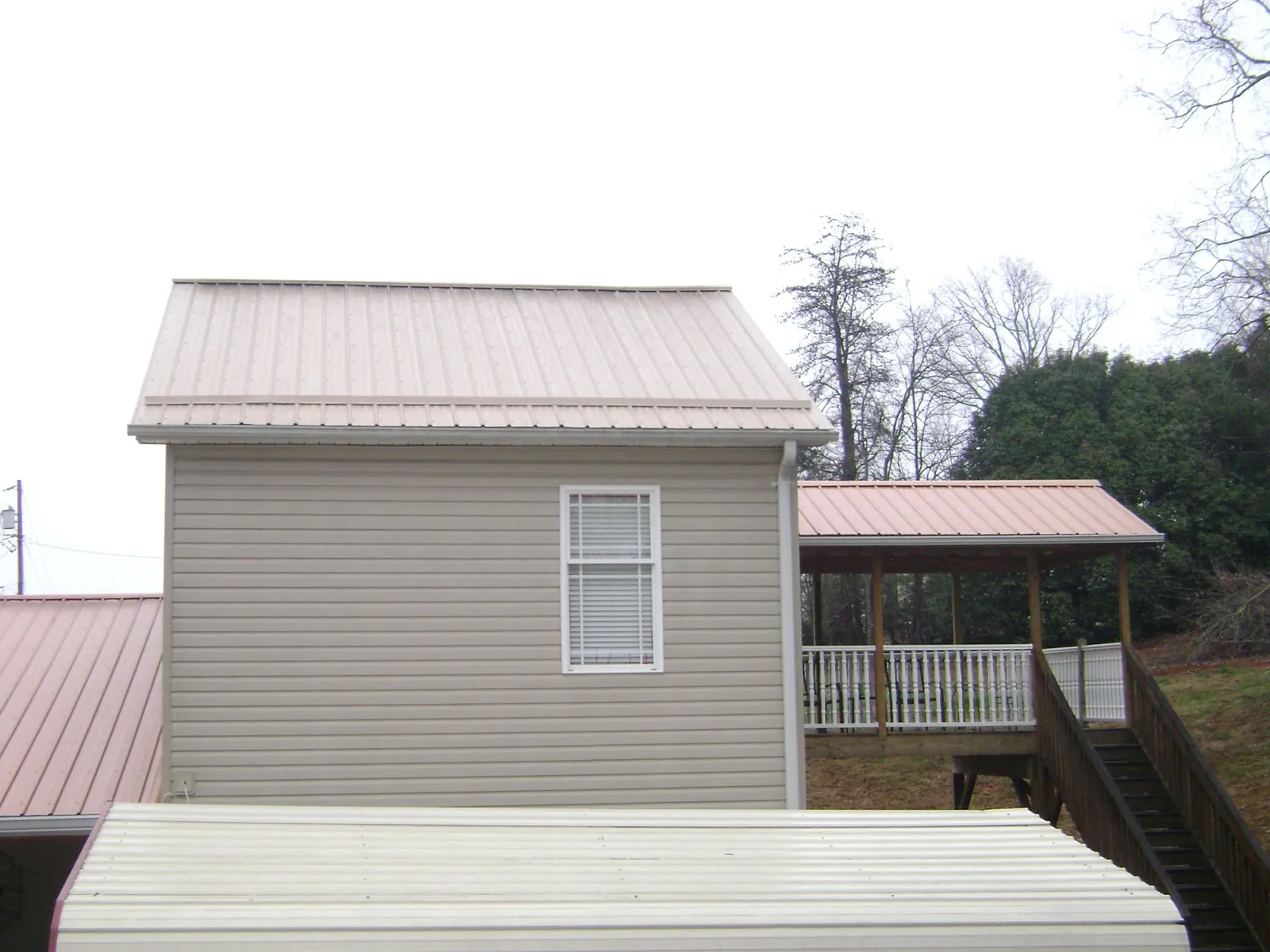 Tan metal roofs on a two story addition and attached porch, from a Roof Replacement job in Five Points